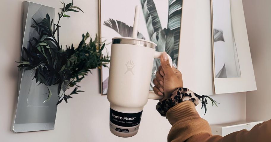 hand holding 32oz Hydro Flask Travel Tumbler Stainless Steel Vacuum Insulated Tumbler in front of picture and plant