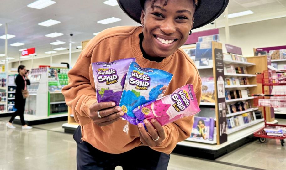 woman holding 3 bags of kinetic sand in a store