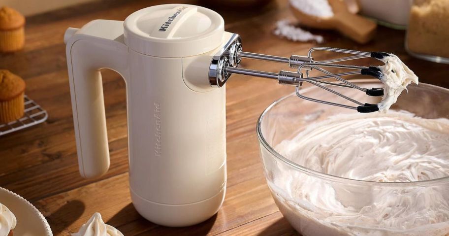 KitchenAid Cordless 7-Speed Hand Mixer w/ Flex Edge Beaters with whipped cream on it on counter next to mixing bowl with whipped cream in it