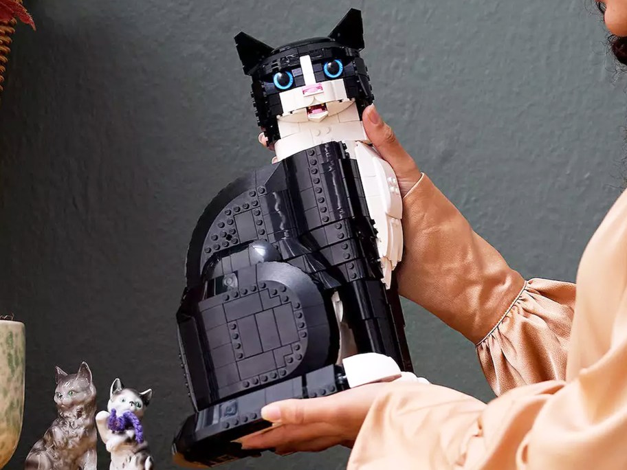 woman holding up a black and white cat made of legos