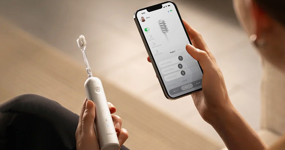 woman holding up electric toothbrush and app on phone
