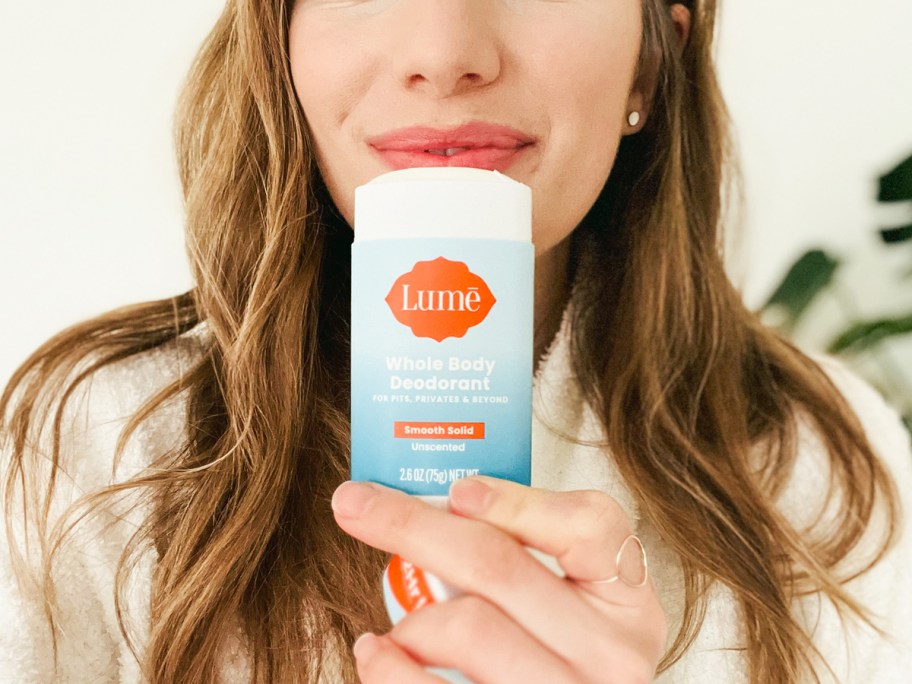 woman holding a stick of lume whole body deodorant up to her face