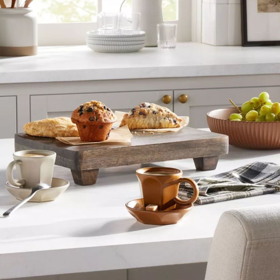 a wooden footed serving tray with assorted food on it, placed on a kitchen counter