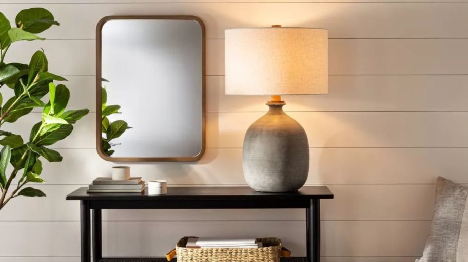 A gray table lamp on a console table next to a chair.