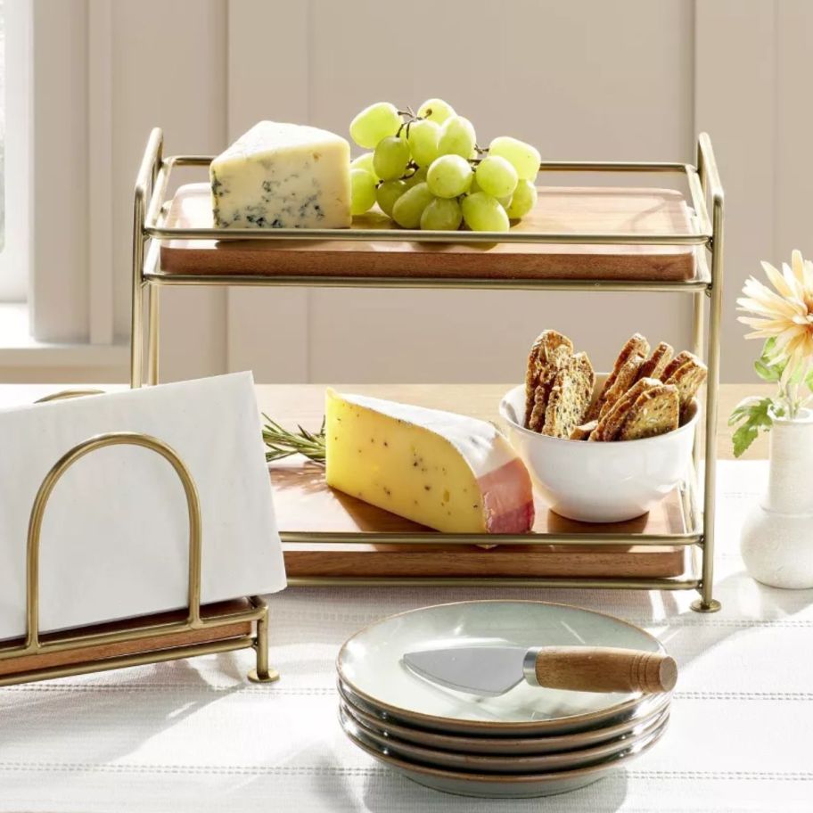 A tired wood and brass serving tray with cheese and grapes on it.