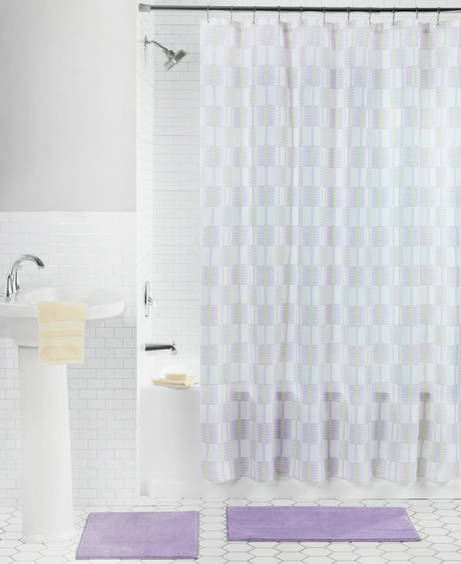 white and purple shower curtain in bathroom with purple rugs on floor
