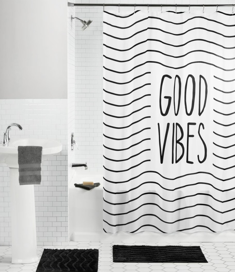 black and white shower curtain that says "good vibes" with 2 black rugs on floor