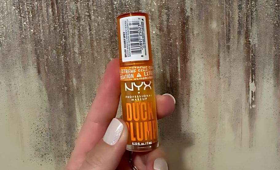 a womans hand holding a tube of nyx duck plump plumping lip gloss