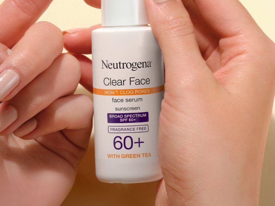 hands holding Neutrogena Clear Face Serum SPF 60 Sunscreen w/ Green Tea 1.7oz