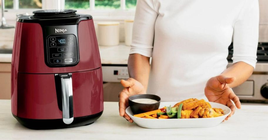 A woman with Buffalo wings and a Ninja 4-Quart Air Fryer in Red 