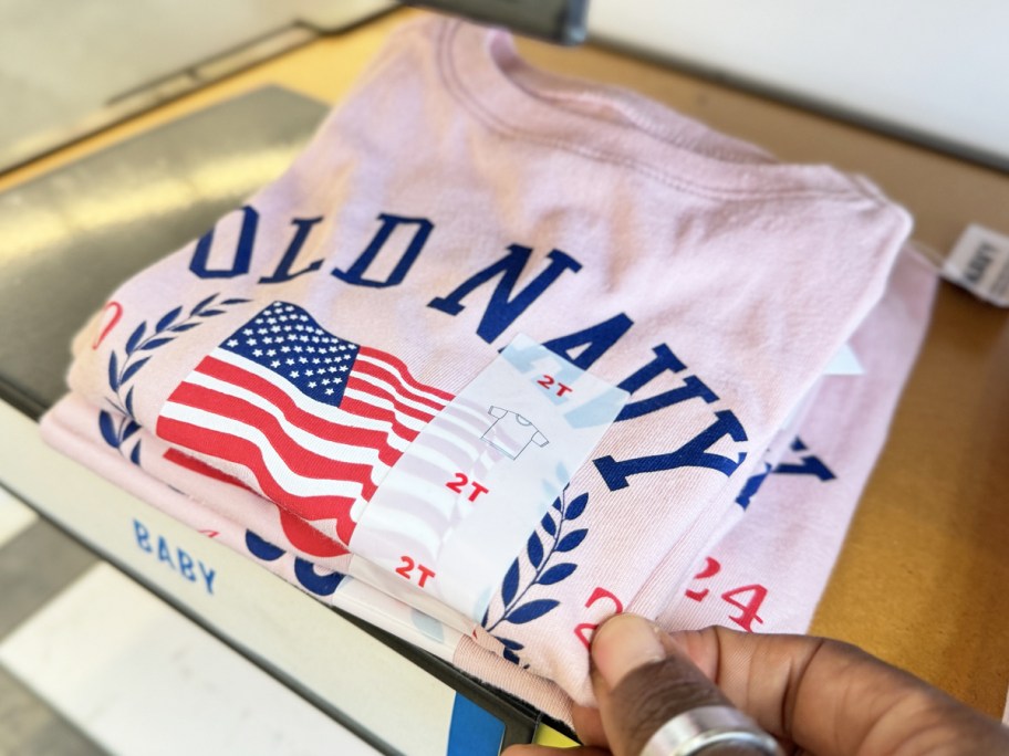 hand touching pink old navy flag tee on shelf