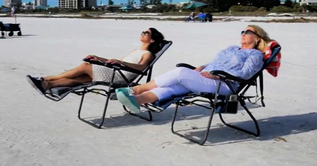 2 women laying on outdoor lounger chairs on beach