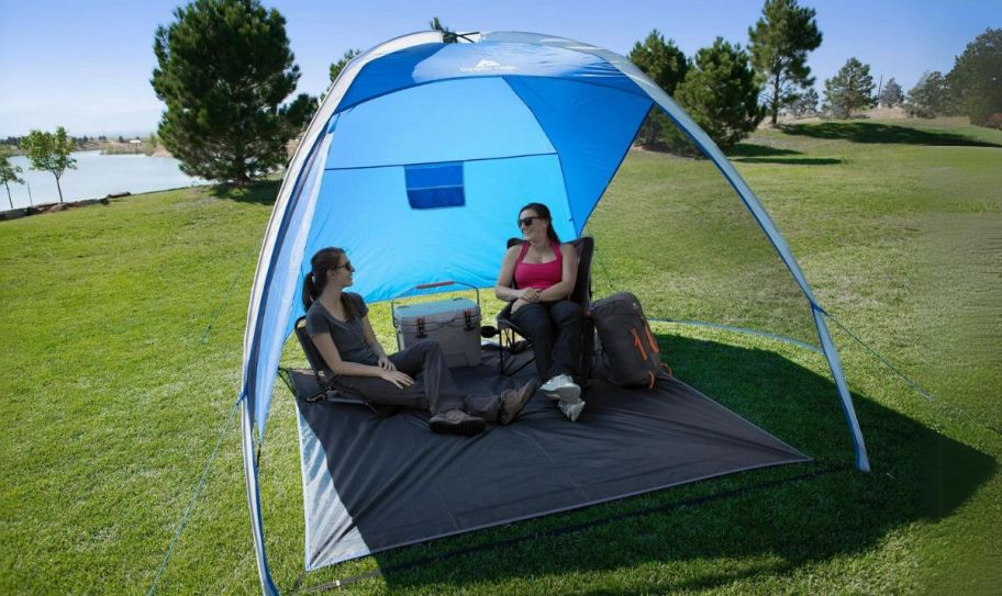 two women lounging camping chairs under a beach tent 