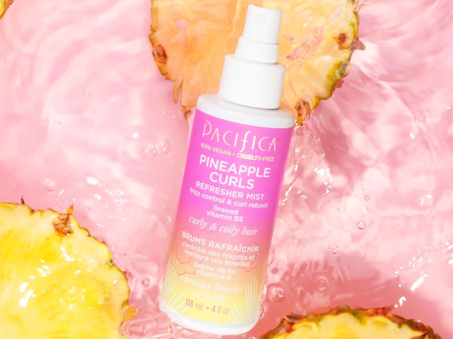 pink bottle of Pacifica Pineapple Curls Refresher Mist in water with cut pineapples