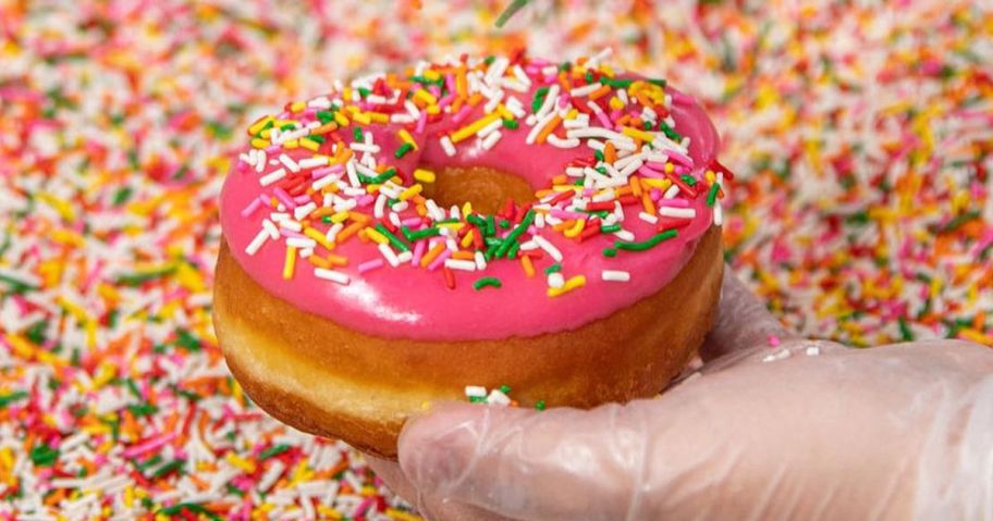 Hand putting Sprinkles on a Pink Frosted Doughnut
