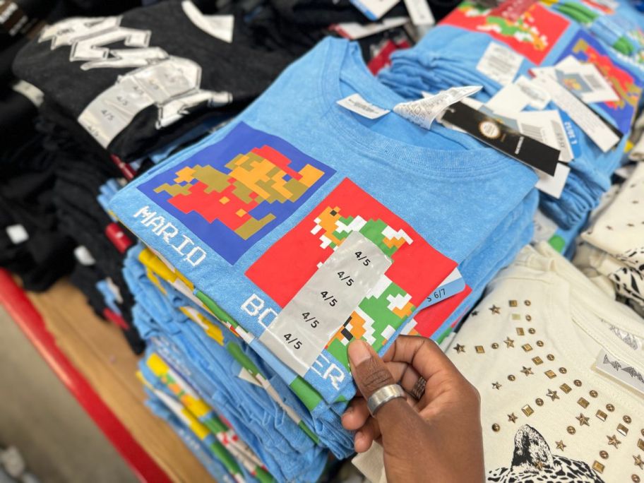 A hand holding a Mario tee shirt in a store