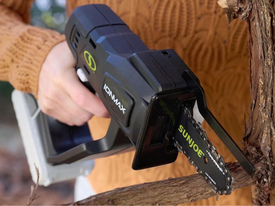 Hand using a Sun Joe handheld chainsaw to cut a tree
