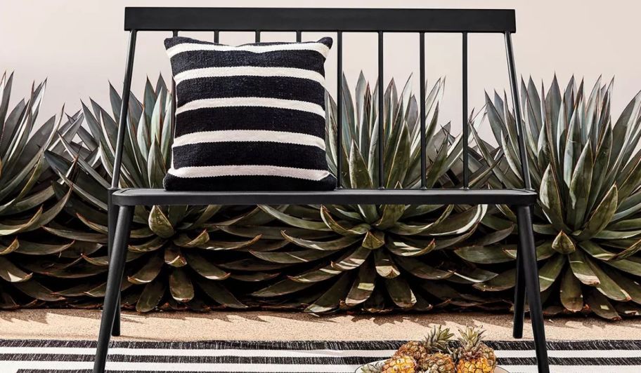 a black metal patio bench shown with a black and white striped throw pillow
