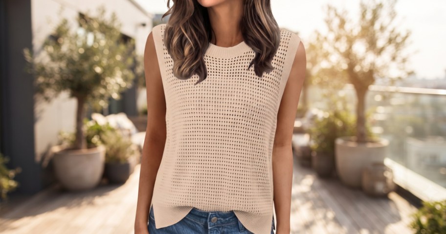A woman wearing a beige knit crochet sleeveless top and blue jeans outdoors on a sunny patio.