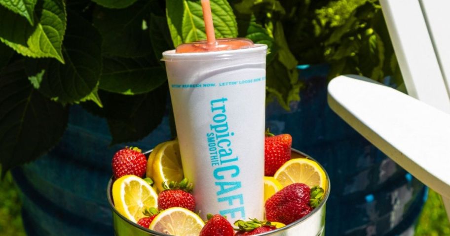 A bucket of strawberries and lemons with a smoothie from Tropical Smoothie Cafe inside of it