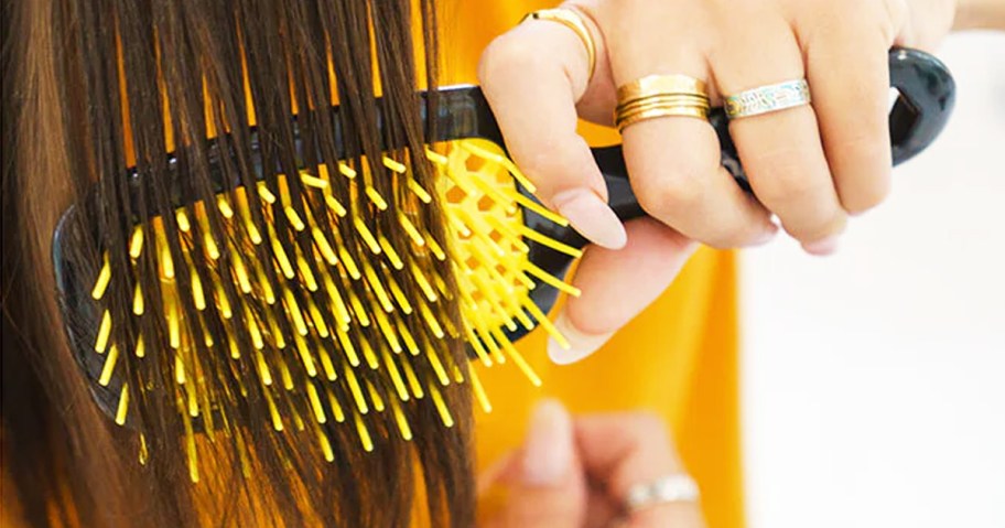 woman using black and yellow hairbrush on her brown hair