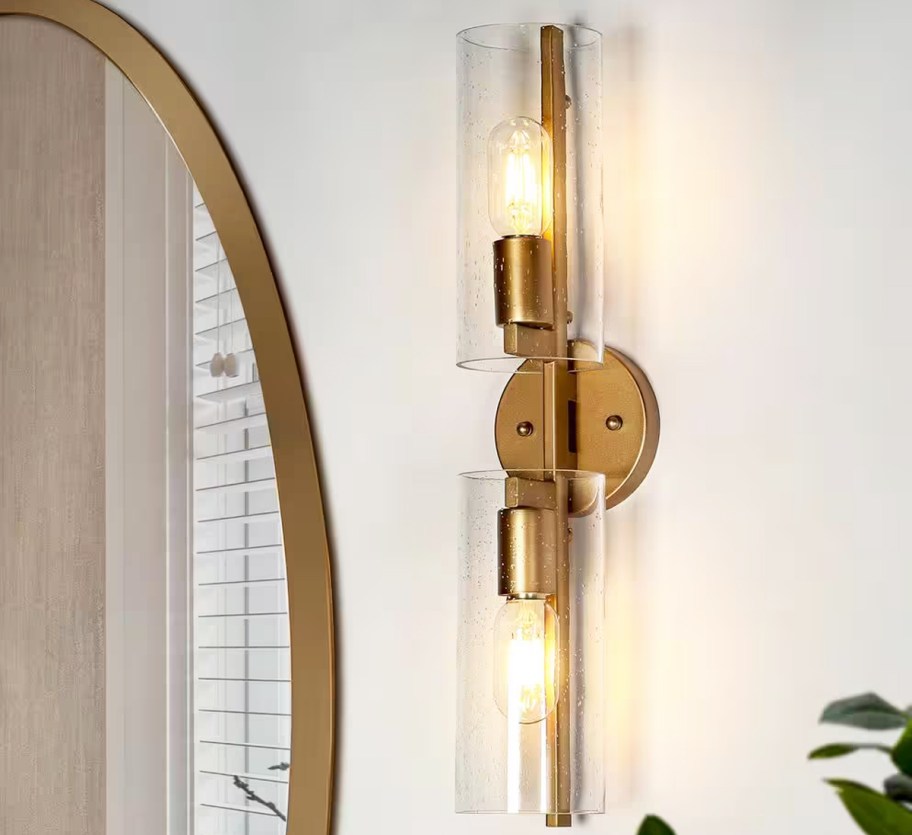 gold vertical light fixture on side of gold wall mirror