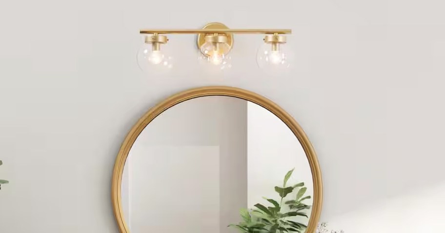 gold vanity light above round gold mirror