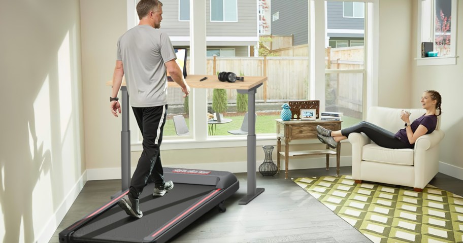 man using an under-desk walking treadmill in front of window 