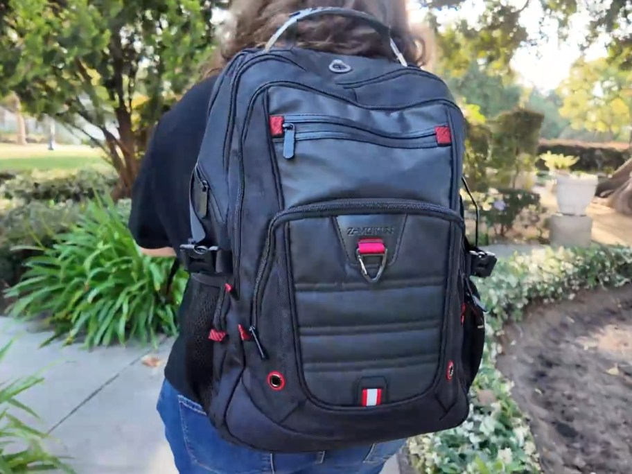 person walking outdoors wearing a large black backpack with red accents