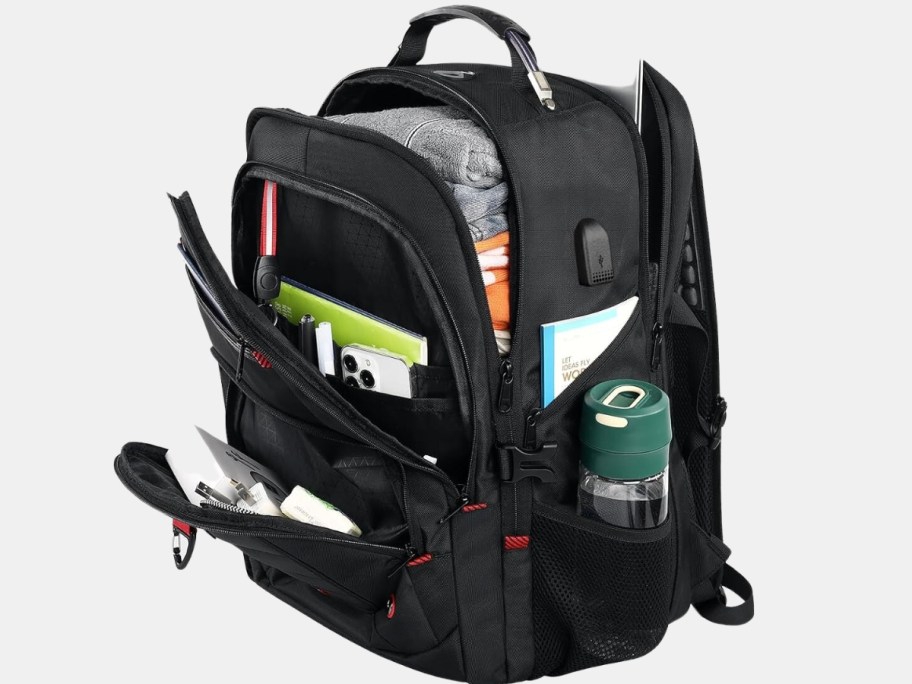 large black packpack shown open filled with various clothing, tech, personal care, papers and a water bottle.