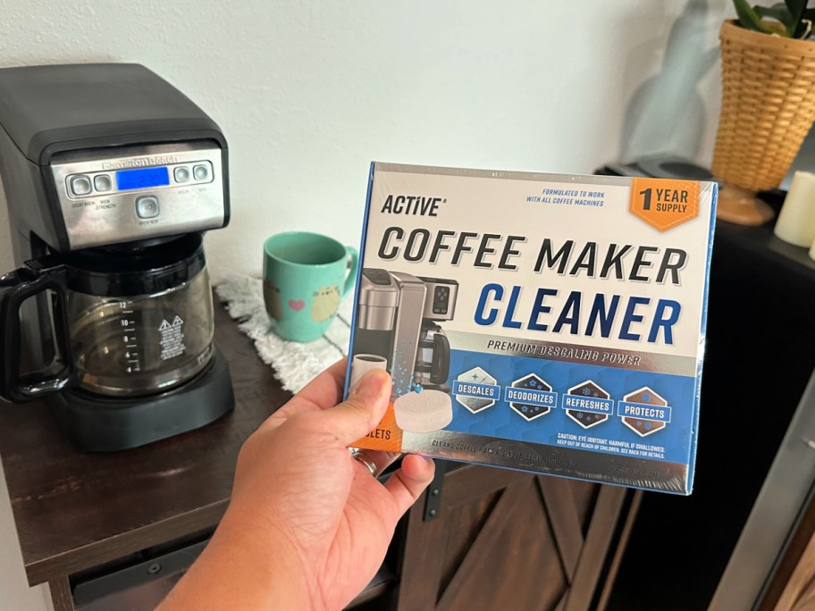 man holding up an active coffee maker cleaner box next to a coffee maker