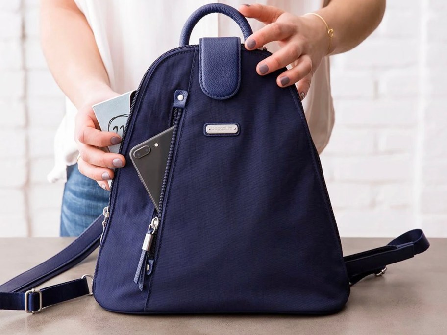 woman putting phone and other items into navy backpack 