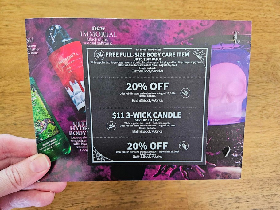 hand holding a bath and body works halloween coupon mailer up close