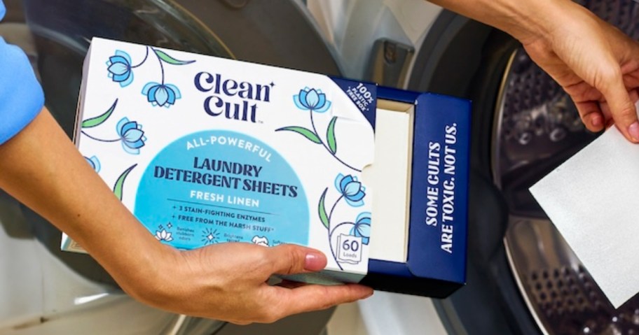 person holding a box of Cleancult Laundry Detergent Sheets and placing 1 into a washer