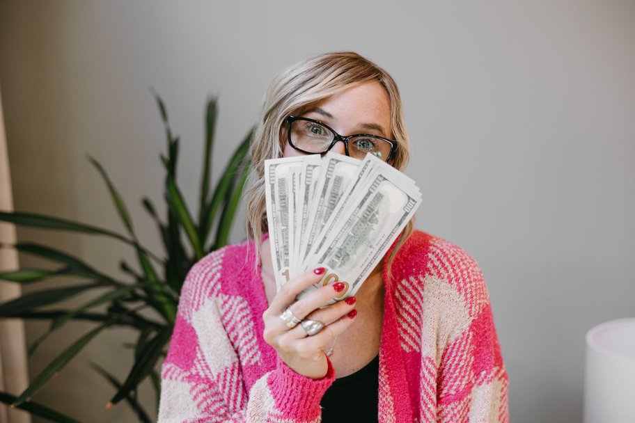 woman in pink plaid sweater holding stack of money