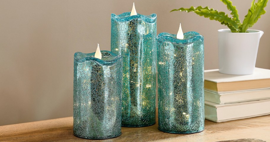 three teal crackle glass candles on table next to books and plant