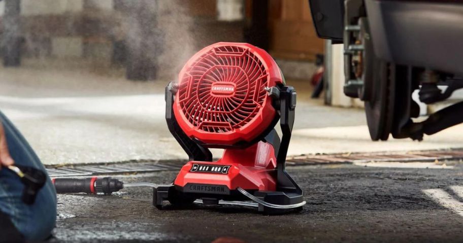 CRAFTSMAN 7.5-in 20-Volt 3-Speed Outdoor Red Misting Personal Fan on ground next to man working on car