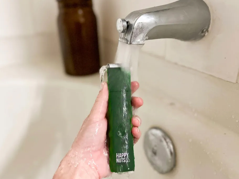 hand holding personal trimmer under faucet