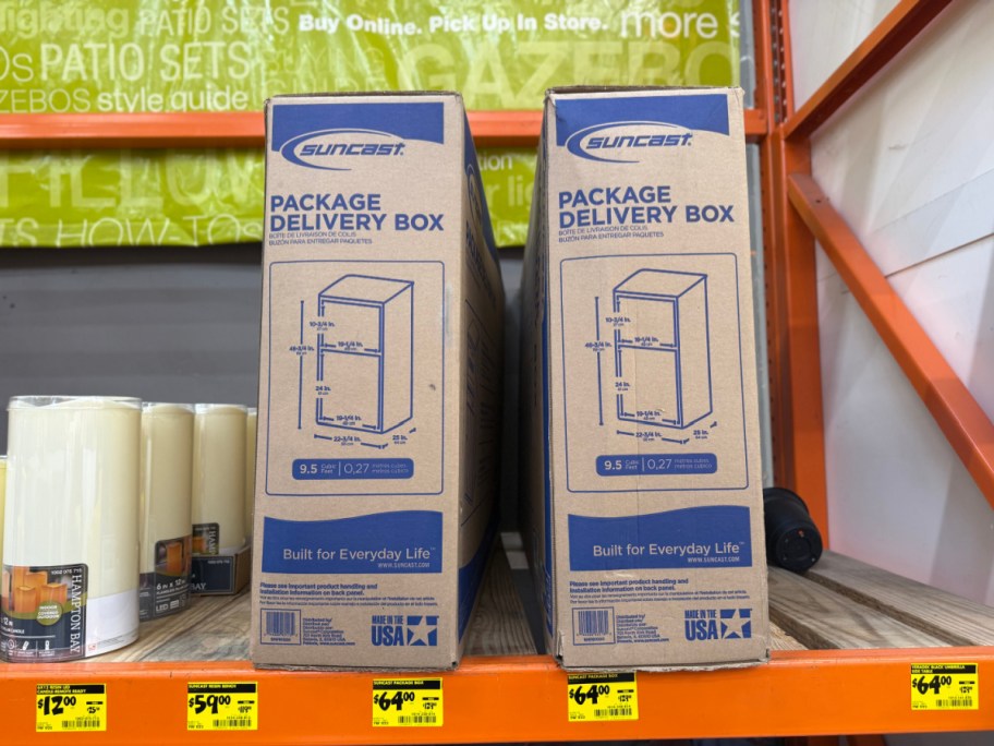 Two cardboard boxes for Suncast Package Delivery Boxes on an orange store shelf above yellow clearance tags.