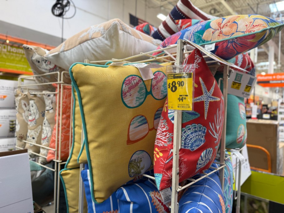 A wire store display rack filled with colorful, summer-themed outdoor throw pillows featuring a yellow $8.90 clearance tag.