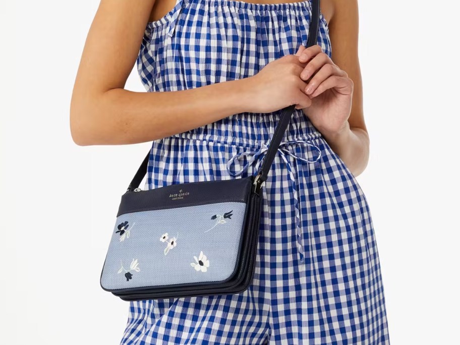 woman wearing a blue and white gingham dress with a blue crossbody bag that has flowers on it