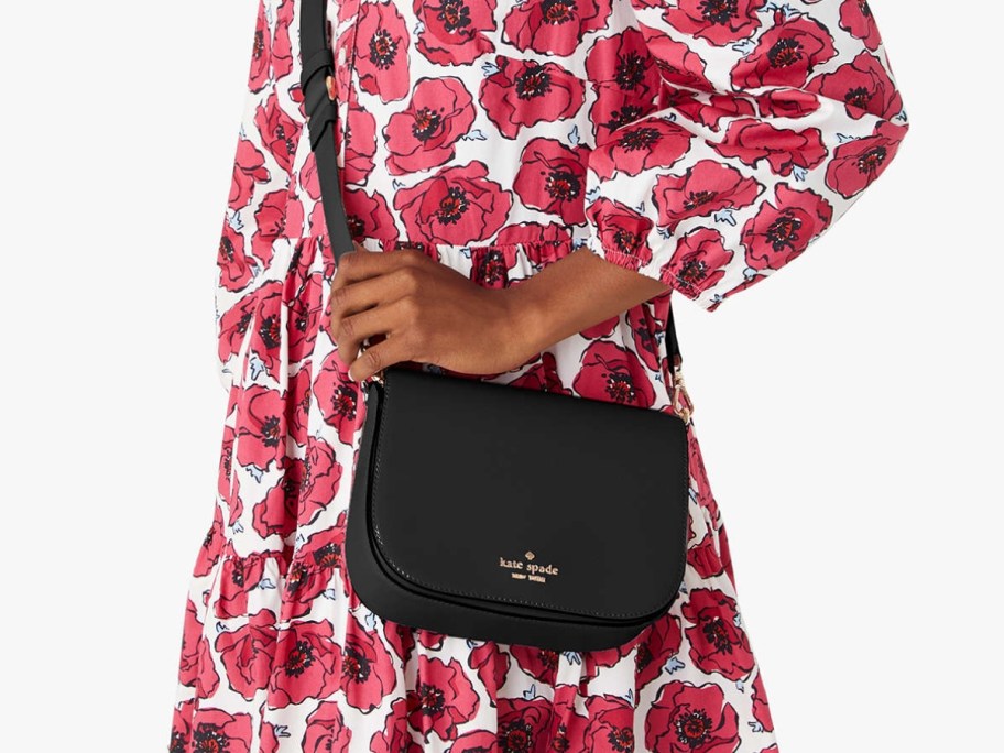woman wearing a dress with red poppy flowers on it, carrying a black Kate Spade crossbody bag