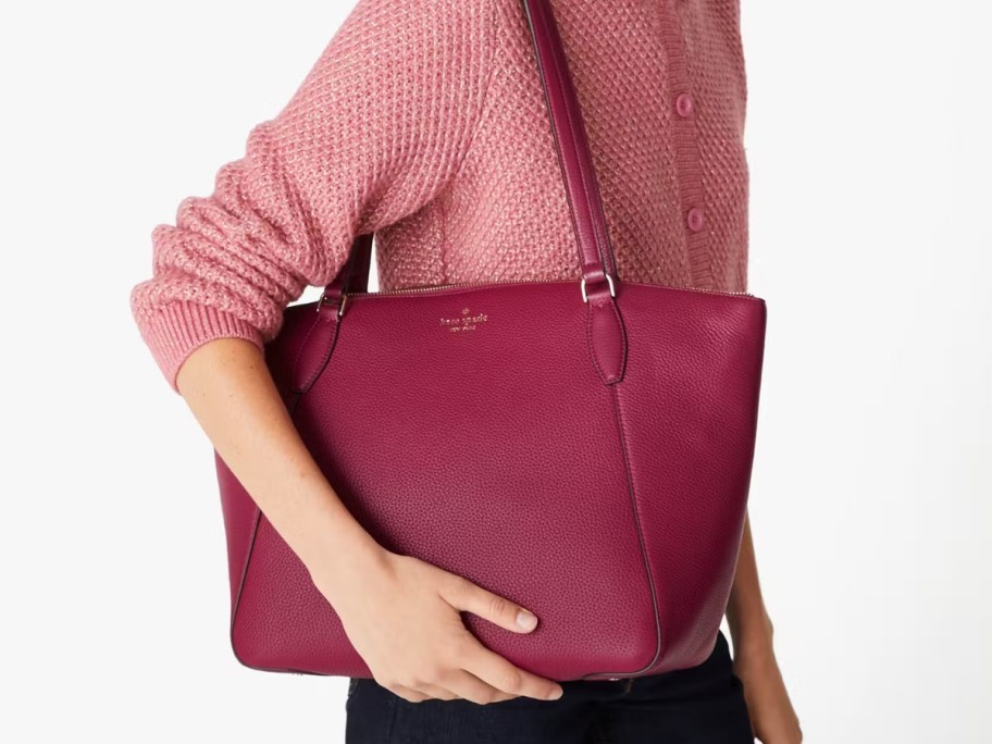 woman wearing a pink top and carrying a large maroon color Kate Spade tote bag