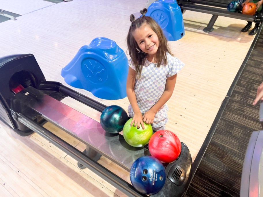 girl standing in front a bowling ball return machine