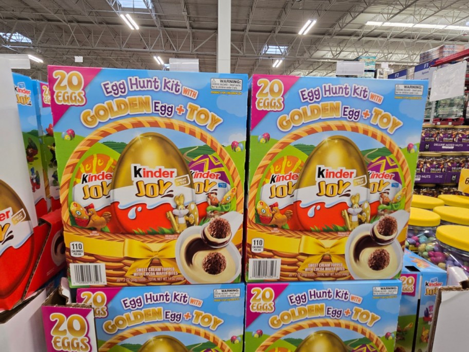 Kinder Joy Egg Hunt Kits are stacked on a store shelf. The colorful boxes feature a golden egg and promise toys inside.