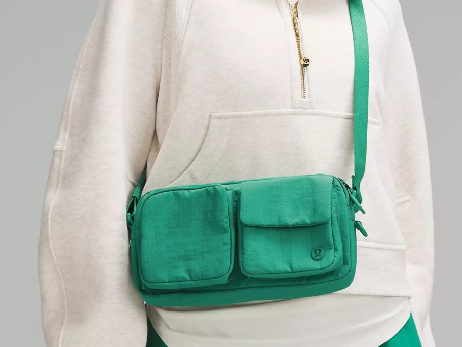 woman wearing a whit quarter zip hoodie with a green lululemon Multi-Pocket Crossbody bag