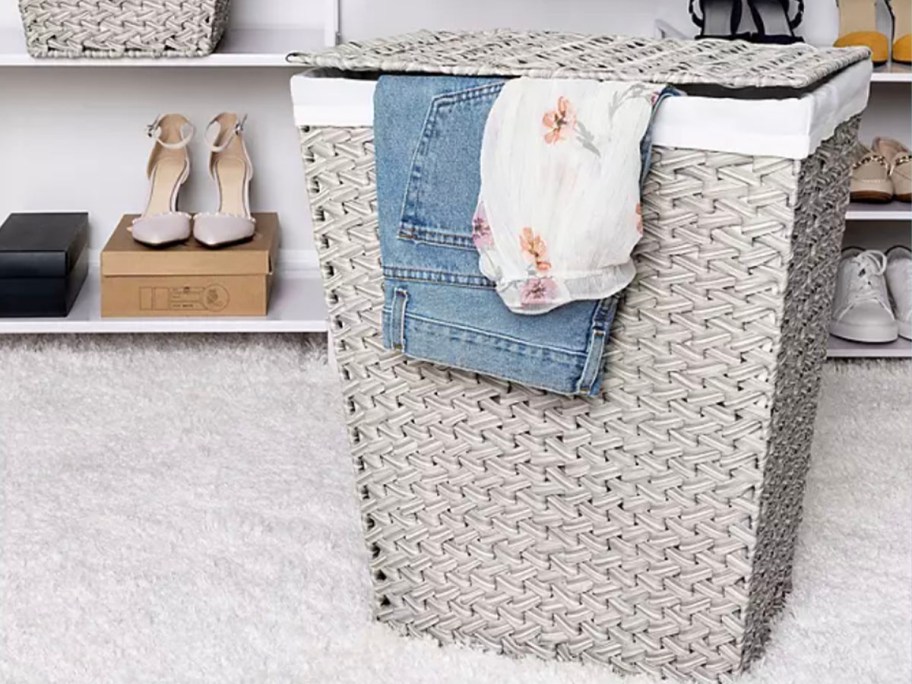 gray wicker laundry hamper with clothes hanging out in room 