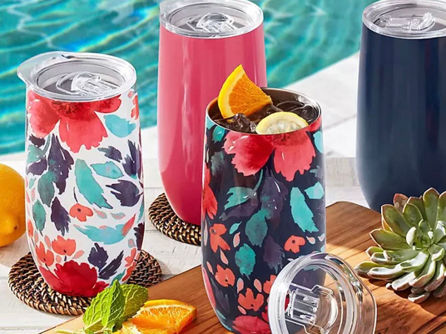 floral, pink, and blue stainless steel tumblers sitting next to pool 