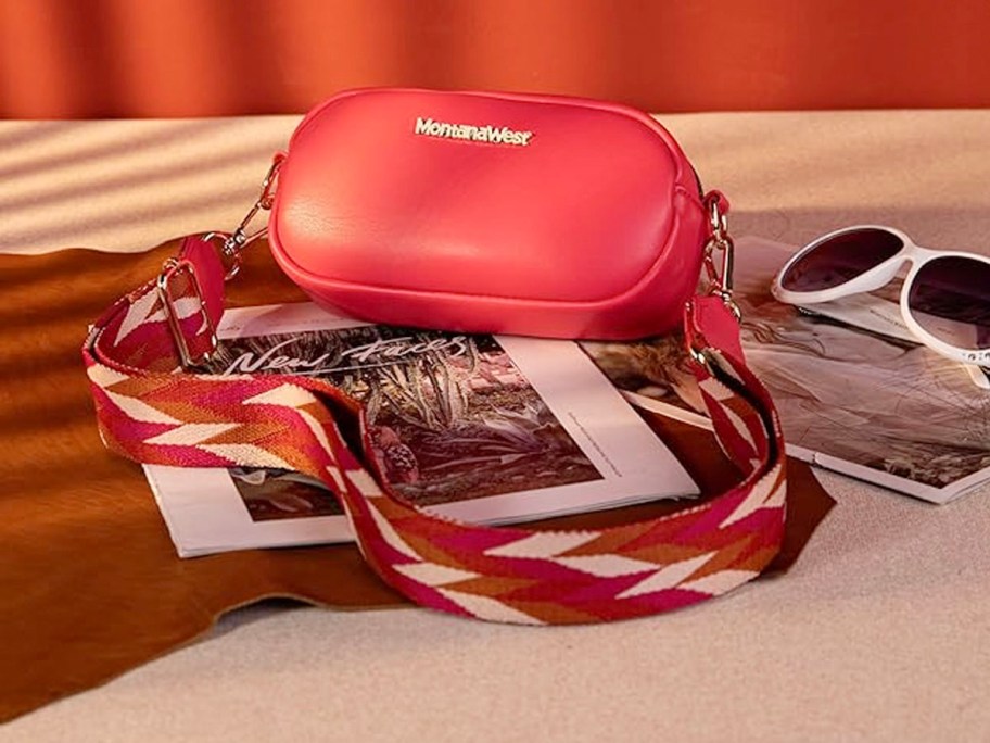 red montana west camera crossbody bag laying on table with sunglasses