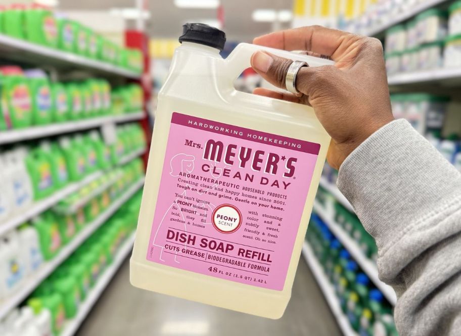 a womans hand holding a bottle of mrs meyers dish soap refill